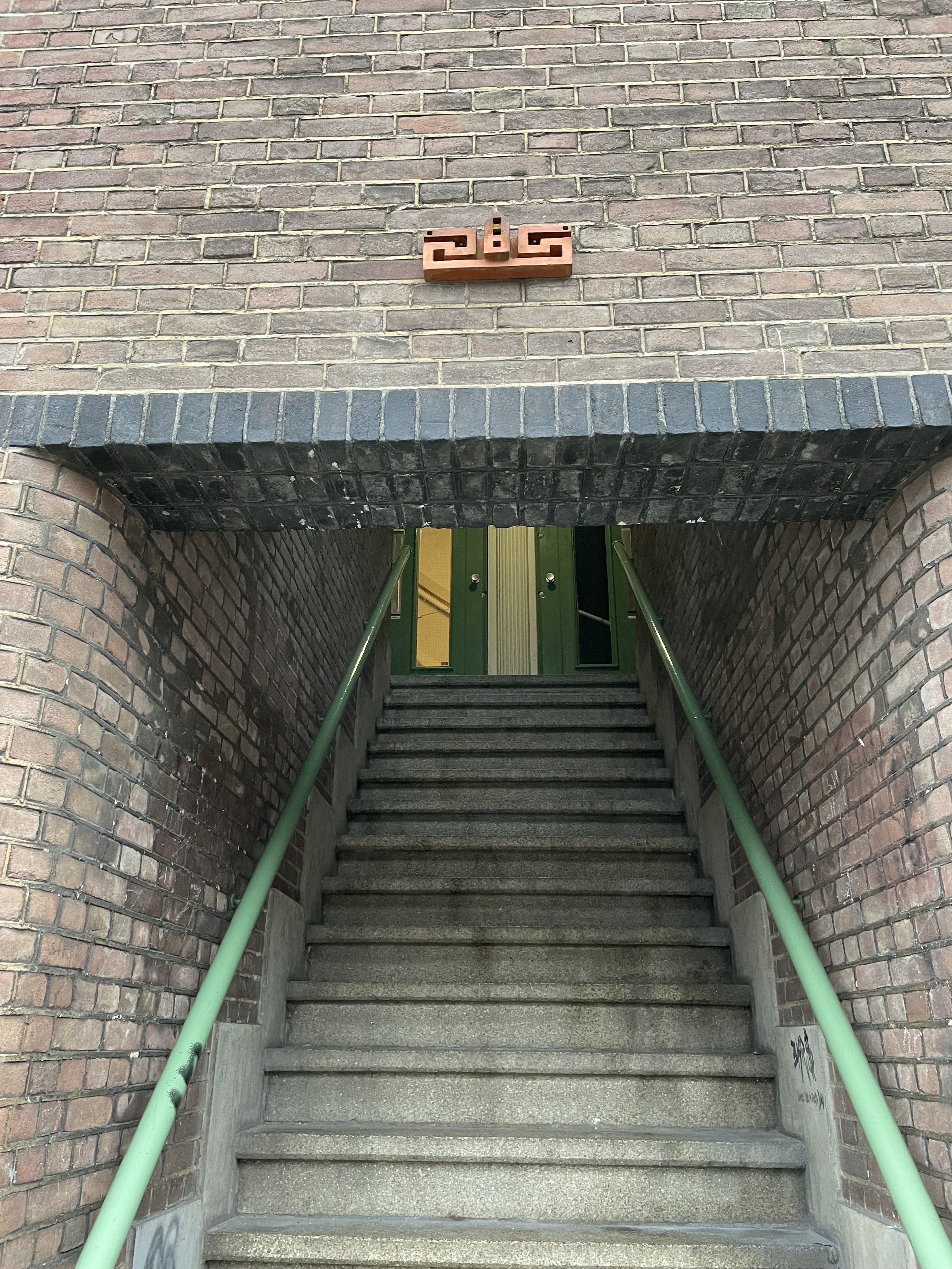 A picture of a building with a little terracotta structure above the entryway that looks like a tiny building with three towers and multiple windows.