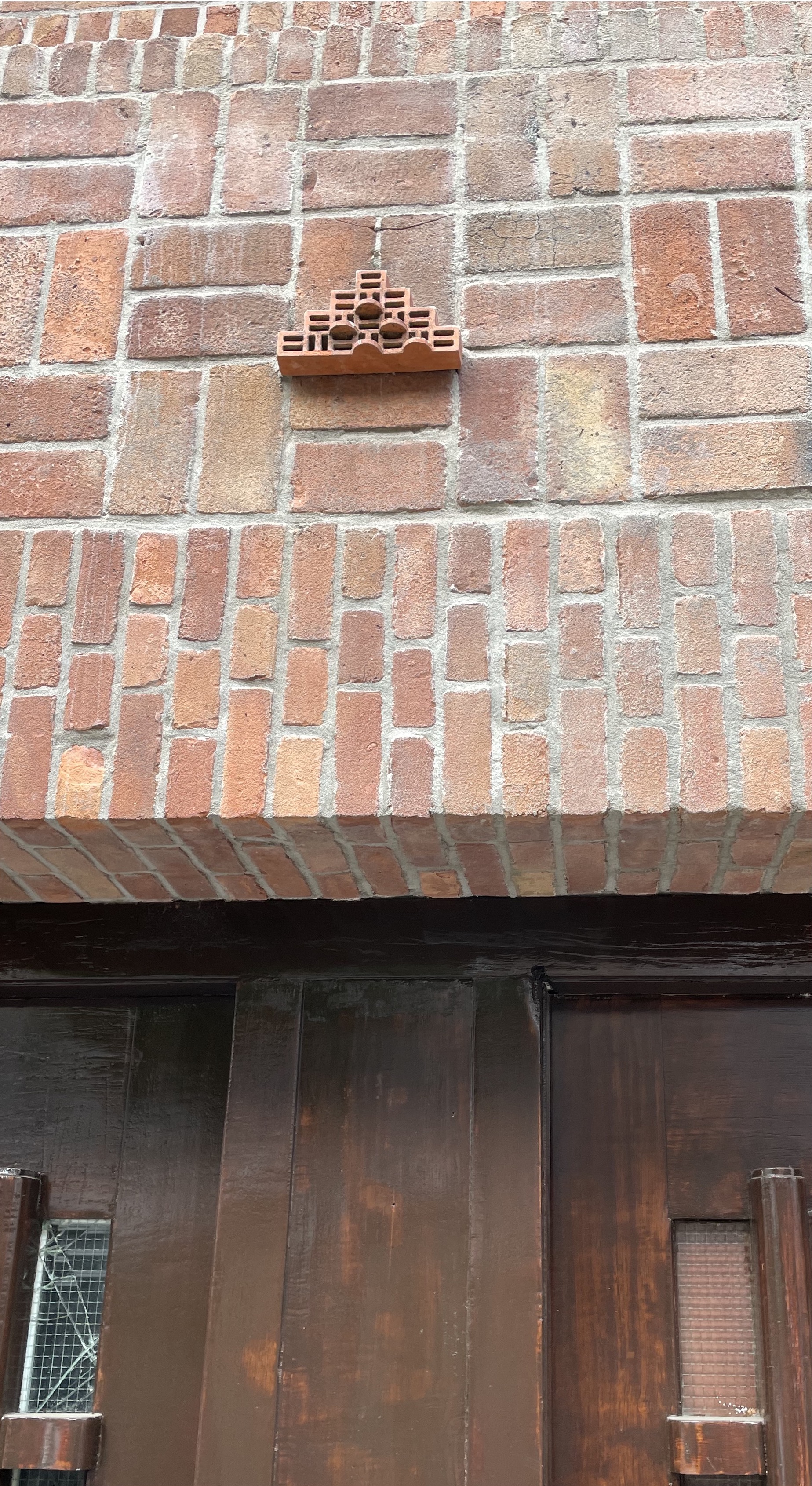 A picture of a building with a little terracotta structure above the entryway that looks like an Aztec structure with blocky lines that fold back over themselves like snakes.