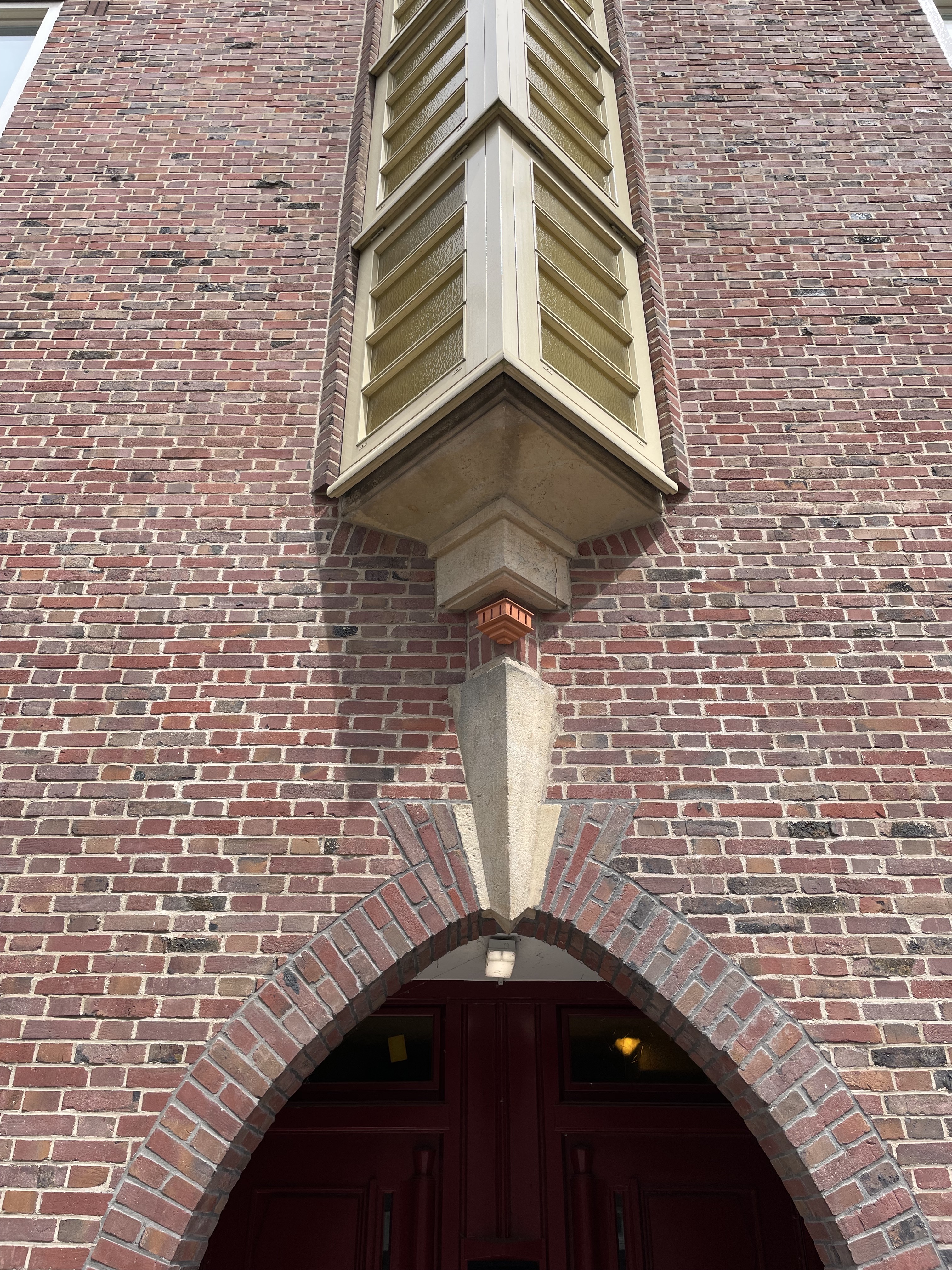 A picture of a building with a little terracotta structure above the entryway that looks like a tiny structure, smaller than a birdhouse that matches the style of the building and windows it sits on.