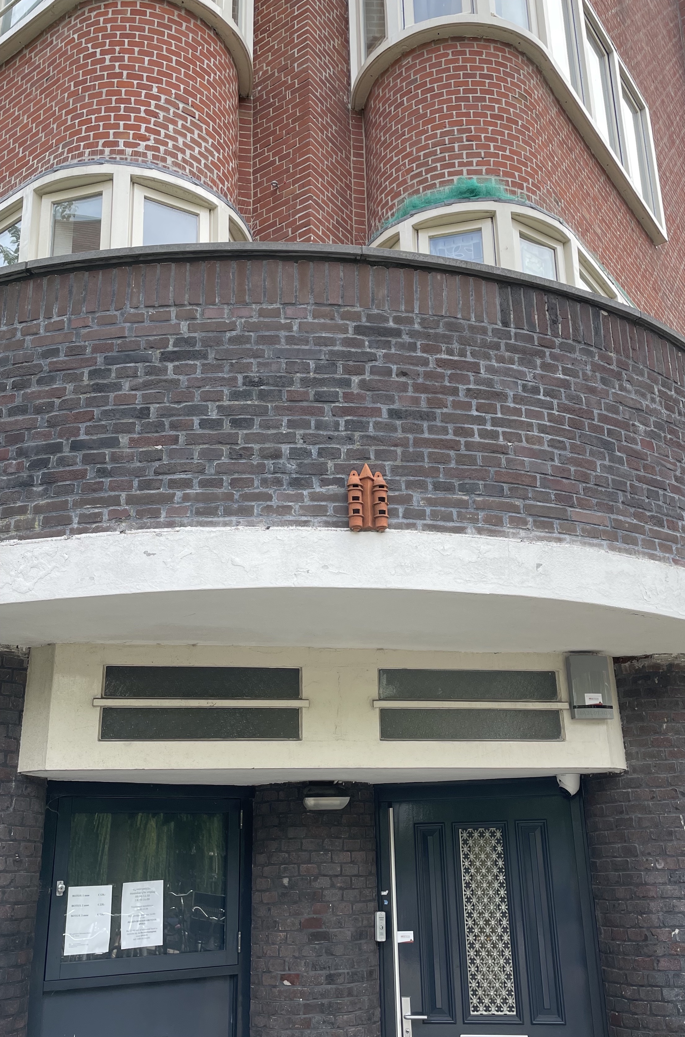 A picture of a building with a little terracotta structure above the entryway that looks like a tiny building with three towers and multiple windows.